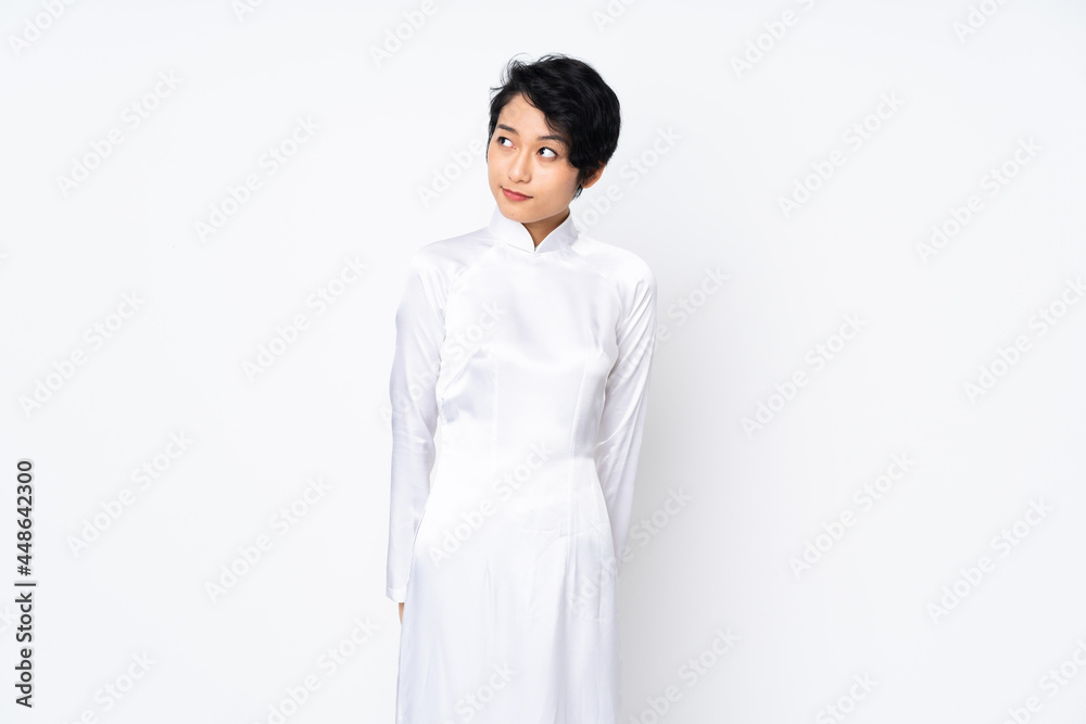 Young Vietnamese woman with short hair wearing a traditional dress over isolated white background making doubts gesture looking side Young Vietnamese woman with short hair wearing a traditional dress over isolated white background making doubts gesture looking side