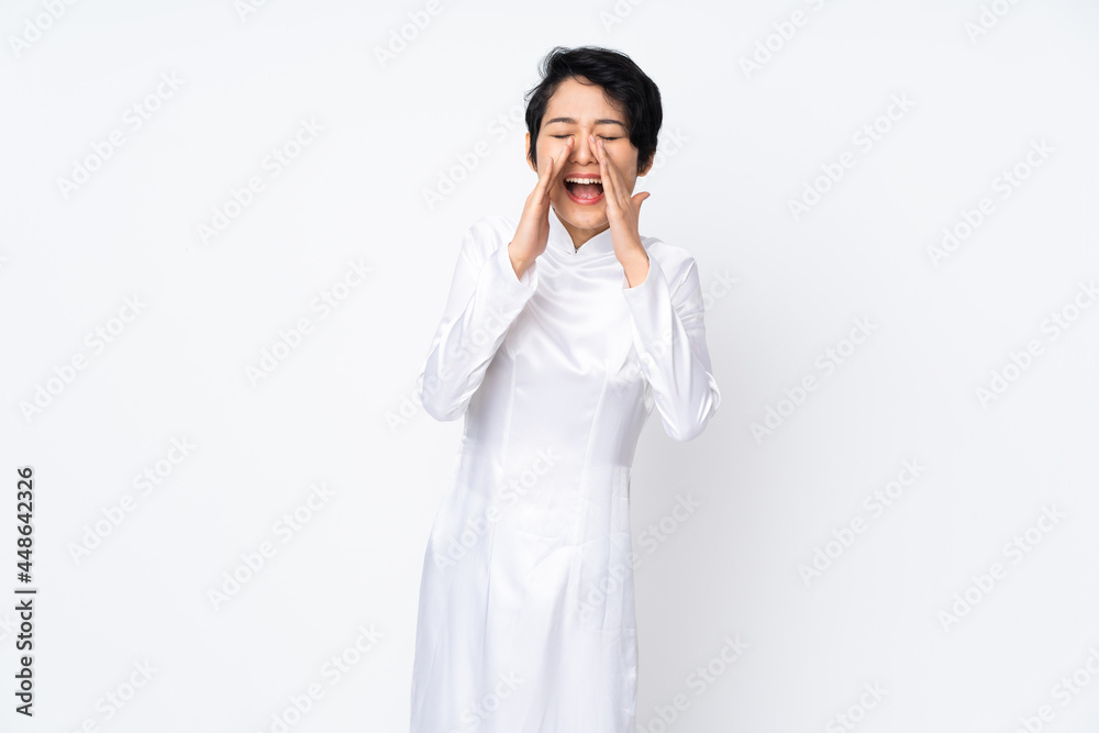 Young Vietnamese woman with short hair wearing a traditional dress over isolated white background shouting and announcing something Young Vietnamese woman with short hair wearing a traditional dress over isolated white background shouting and announcing something