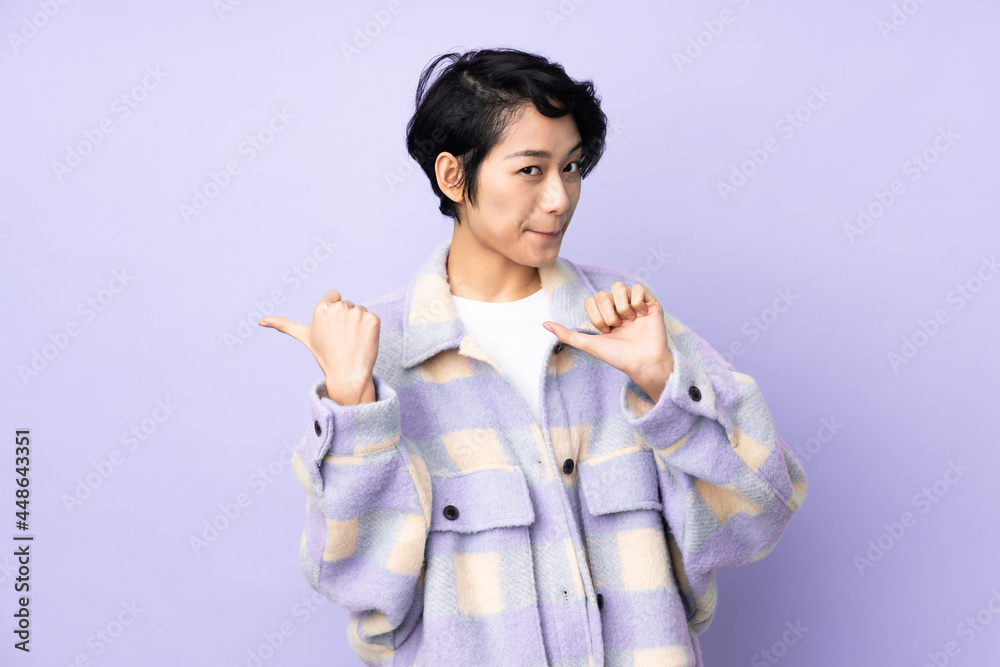 Young Vietnamese woman with short hair over isolated background pointing to the side to present a product Young Vietnamese woman with short hair over isolated background pointing to the side to present a product