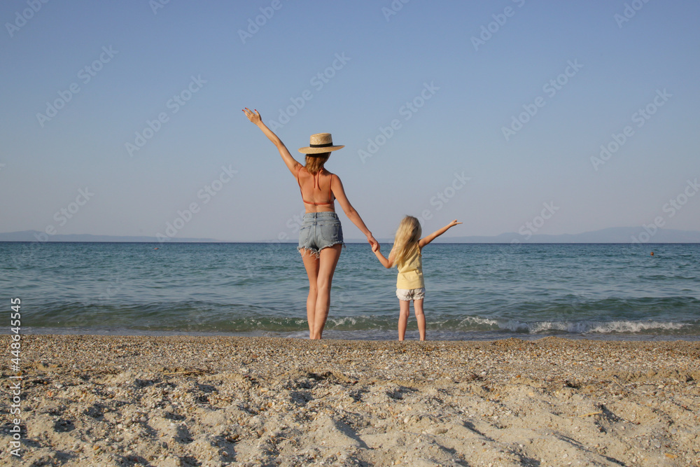 Mother and daughter on the beach looking to horizon over the sea with hands raised up. Family summer vacation concept. Mother and daughter on the beach looking to horizon over the sea with hands raised up. Family summer vacation concept.