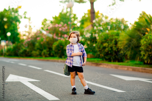a beautiful little girl, a schoolgirl, is standing on the road, with a backpack, holding a diary in her hands