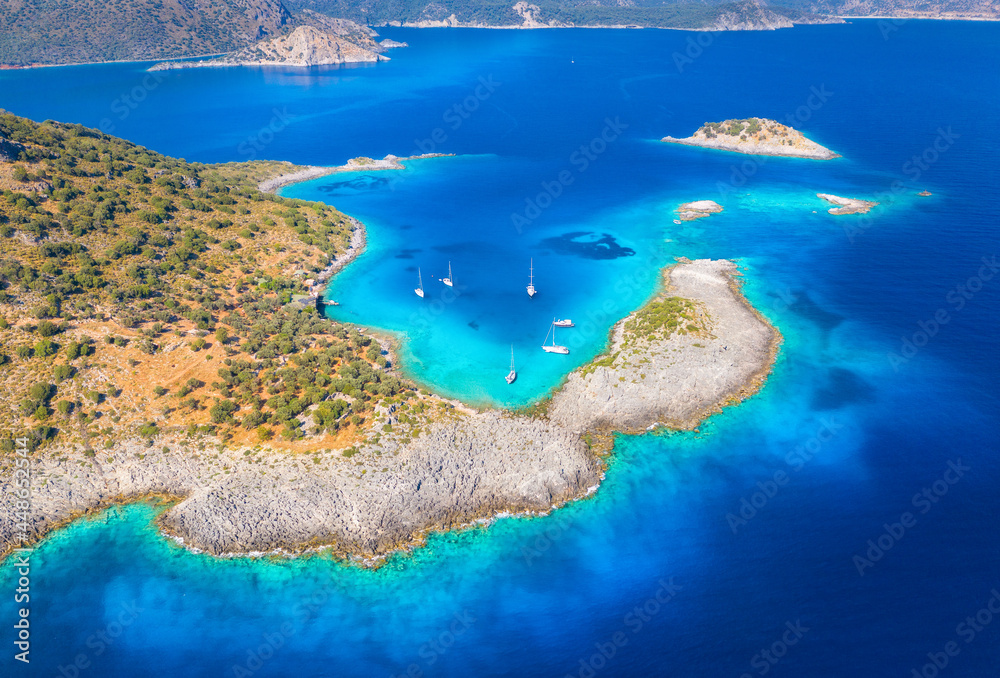 Aerial view of beautiful sea bay, yachts and boats at sunset in summer. Akvaryum koyu in Turkey. Top view of luxury yachts, sailboats, lagoon, clear blue water, rock, mountain and green trees. Travel