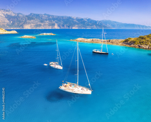 Aerial view of beautiful yachts and boats on the sea at sunset in summer in Turkey. Top view of luxury yachts, sailboats, clear blue water, rocks, sky, mountain and green trees. Travel. Landscape