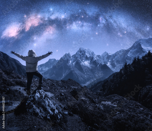 Arched Milky Way, sporty man on the stone and mountains in snow at starry night. Happy young man, sky with bright stars, snowy rocks in Nepal. Space. Landscape with milky way arch. Travel and hiking