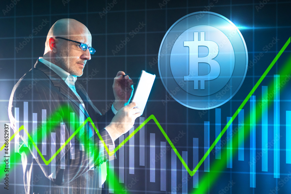 Man is engaged in bitcoin trading. Graph shows exchange rate for bitcoin trading. Adult investor next to bitcoin logo. Trader holds a tablet computer in his hands. He analyzes cryptocurrency market Man is engaged in bitcoin trading. Graph shows exchange rate for bitcoin trading. Adult investor next to bitcoin logo. Trader holds a tablet computer in his hands. He analyzes cryptocurrency market