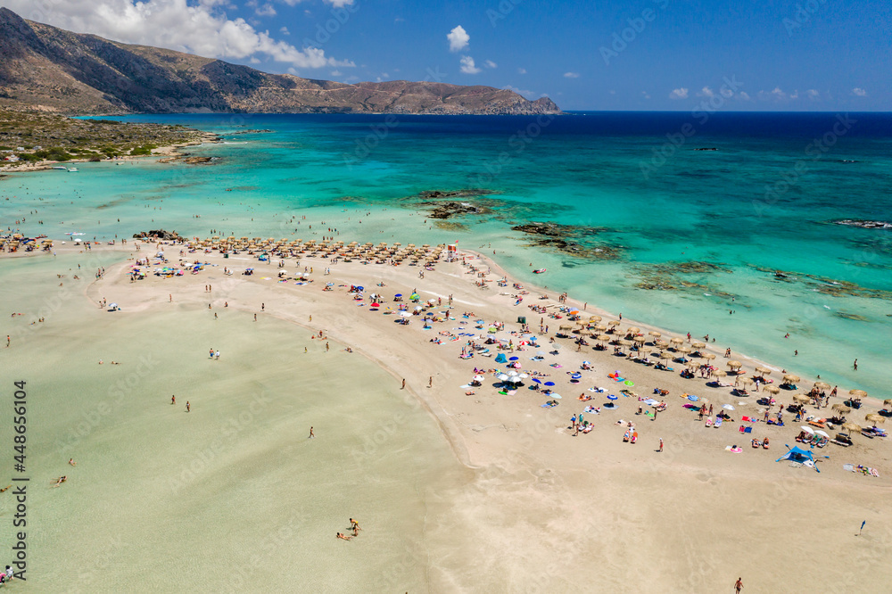 Obraz premium Aerial view of sunshades and umbrellas on a narrow sandy beach surrounded by shallow lagoons (Elafonisso Beach, Crete, Greece)