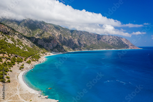 Fototapeta Naklejka Na Ścianę i Meble -  Aerial view of clouds over large mountains on a coastline surrounded by clear, blue ocean (Agia Roumeli, Crete)