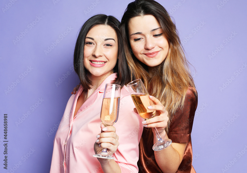 two beautiful women dressed in pajamas drink champagne and have fun over purple background two beautiful women dressed in pajamas drink champagne and have fun over purple background