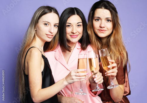 three young beautiful women dressed in pajamas drink champagne and have fun