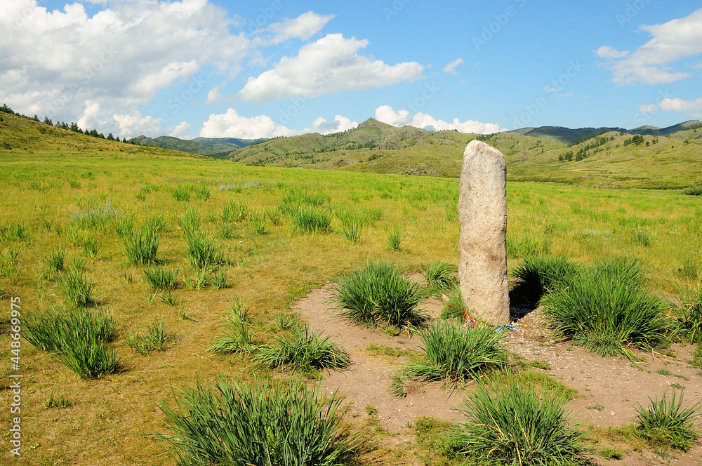 An ancient ritual stone stands in a valley at the foot of a mountain range.