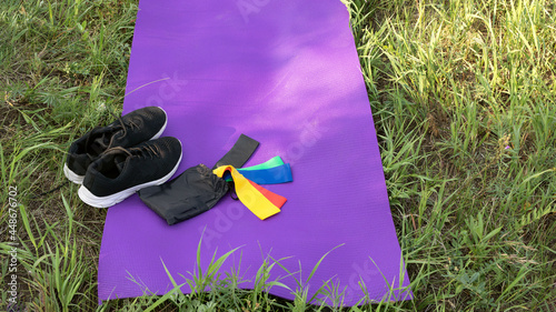 Female sneakers, exersice mat and latex rubber bands on green grass. Spoort equipment or fitness accessories for personal use. Outdoor fitness concept photo