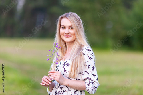 cute blonde woman with a flower in a summer light dress in nature