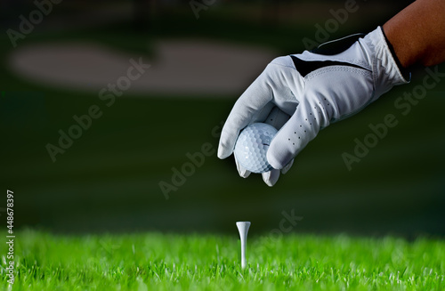 Golfer hold golf ball put on tee by black and white glove with sunlight ray blur green golf course background