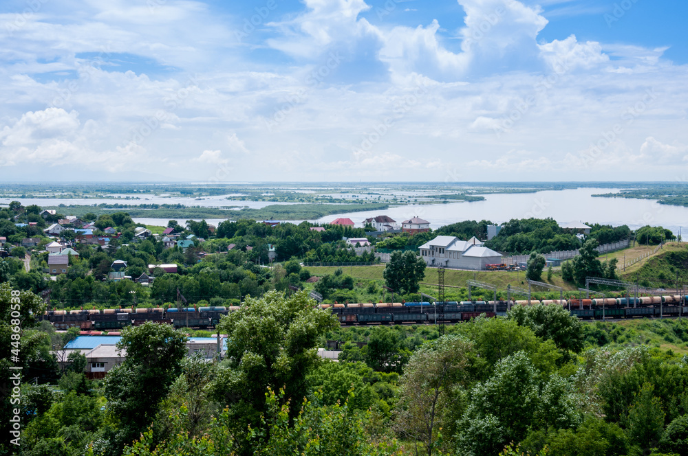 Obraz premium Summer Russian landscape, cottages on the banks of the Amur River and a passing train