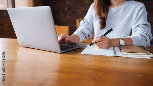 Closeup image of a woman writing on a notebook while working on laptop computer