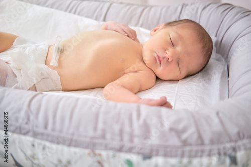 A baby boy sleeps in a cocoon on a cot. A newborn baby in a diaper is lying naked on the bed © Андрей Журавлев