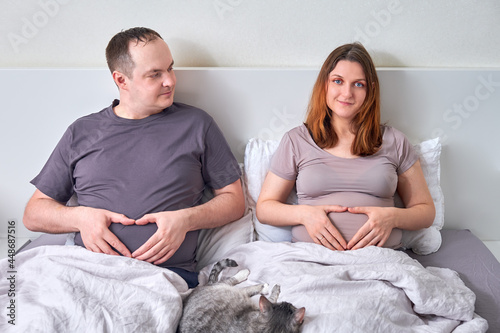 Принти на полотні Pregnant wife and overweight husband lie in bed holding their bellies, concept o