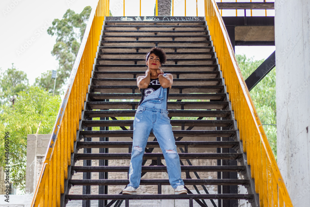 Mid adult afro mexican woman posing on some urban steps with yellow hand rails