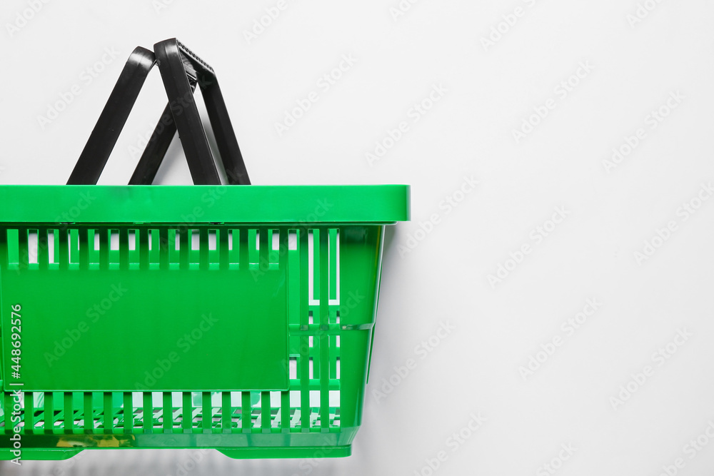 Fototapeta premium Green plastic shopping basket with black handles, retail commerce and consumerism concept, isolated on white background