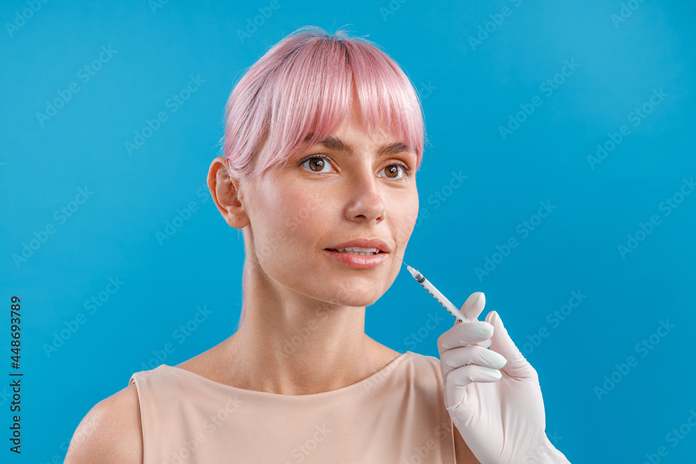 Obraz premium Beautiful woman with pink hair looking away while receiving botox injection in lips from beautician. Beauty concept