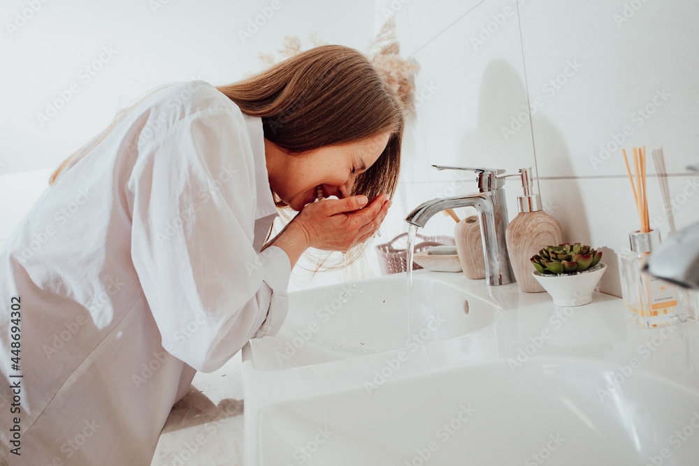 Woman splashing face with water over bathroom sink Woman splashing face with water over bathroom sink