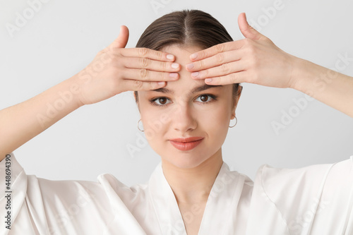 Beautiful young woman massaging her face on light background