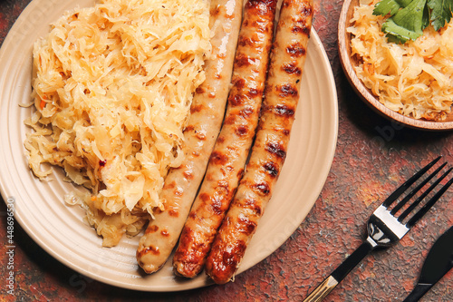 Plate with tasty sauerkraut and grilled sausages on grunge background, closeup