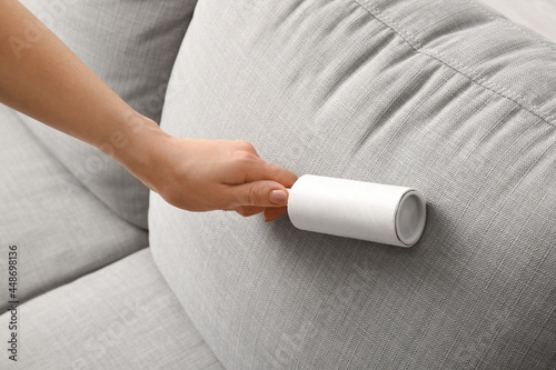 Woman cleaning sofa with lint roller, closeup photo