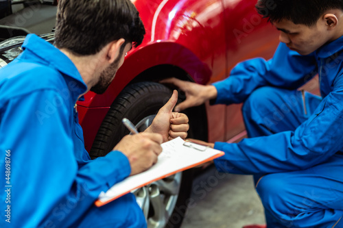 Close up thumbs up hand sign of professional look technician inspecting car underbody and suspension system by using check list in modern car service shop. Automotive business or car repair concept.