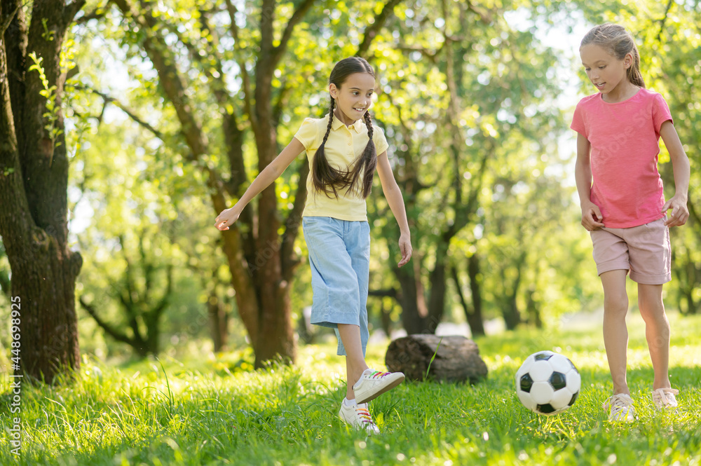 Two younger girlfriends playing soccer on lawn Two younger girlfriends playing soccer on lawn