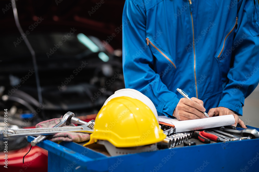 Selective focus on yellow safety helmet of automotive technician staff checking list of repair or service item of vehicle in car service center. Selective focus on yellow safety helmet of automotive technician staff checking list of repair or service item of vehicle in car service center.