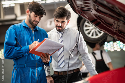 Car service, vehicle repair concept : Car service technician explaining checking list or repaired item to vehicle owner customer after sending car for repairing or check at automobile service center.	 photo