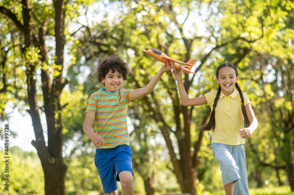 Girl and boy with toy airplane running in park Girl and boy with toy airplane running in park
