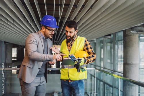Architect and construction worker standing in building in construction process and looking at blueprints on tablet Fotobehang