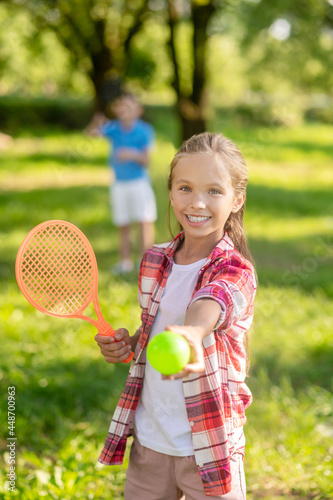 Smiling girl with racket stretching ball forward
