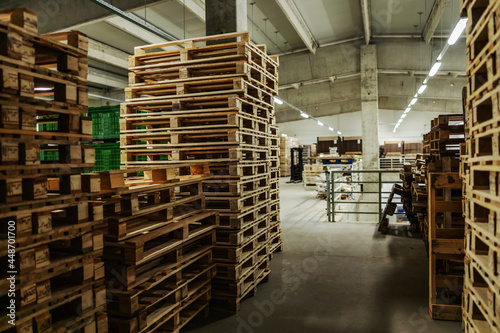 Bunch of wooden pallets in the warehouse. Empty warehouse space with lots of pallets neatly stacked in the factory plant. Indoor warehouse with no people, distribution and logistics, supply