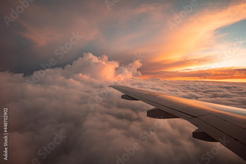 The view from the airplane window to the clouds and sunset. Airplane wing above thick pink and orange clouds. Wonderful breathtaking view