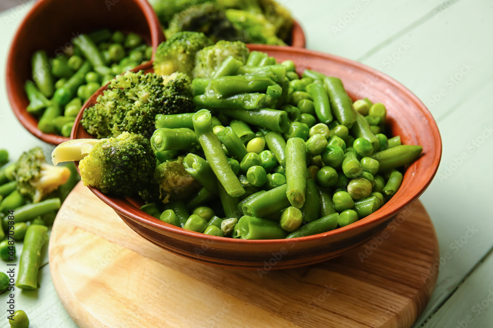 Bowl with frozen green vegetables on color wooden background, closeup Bowl with frozen green vegetables on color wooden background, closeup