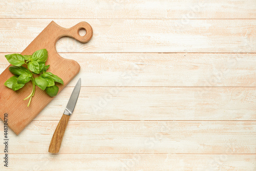 Board with fresh basil and knife on light wooden background