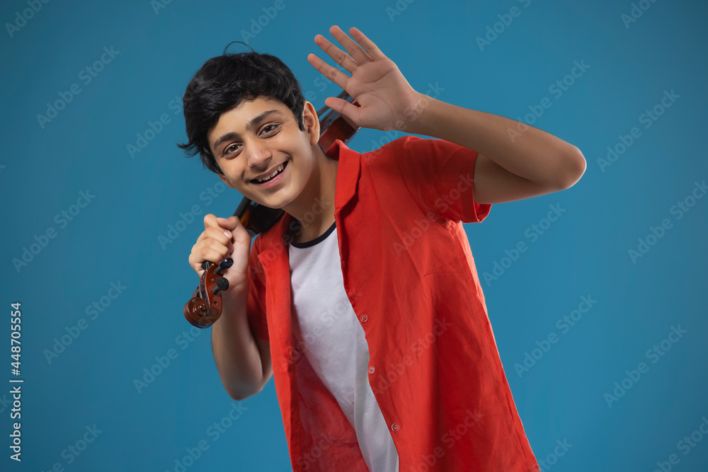 A HAPPY TEENAGER WAVING IN FRONT OF CAMERA WHILE HOLDING VIOLIN