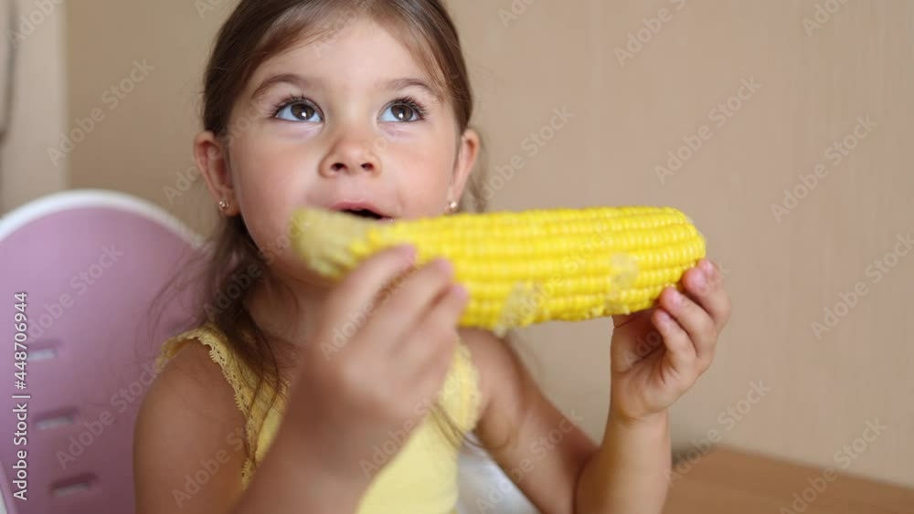 Process of little girl eating fresh cornat home. Adorable kid sits on the table and eats corn appetizing Process of little girl eating fresh cornat home. Adorable kid sits on the table and eats corn appetizing
