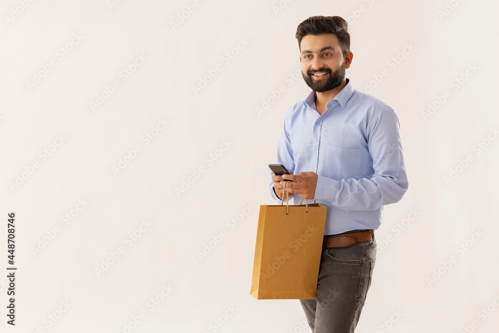 A SMART BEARDED MAN WALKING WHILE HOLDING MOBILE PHONE AND PAPER BAG A SMART BEARDED MAN WALKING WHILE HOLDING MOBILE PHONE AND PAPER BAG