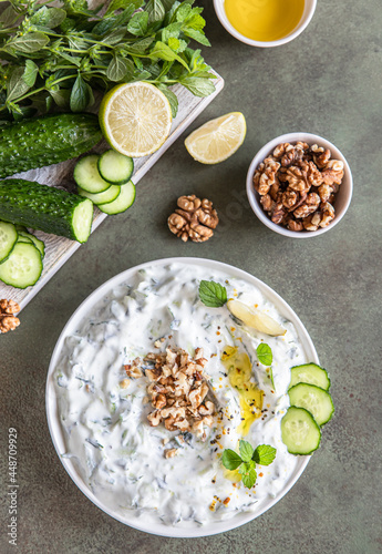 Traditional bulgarian cold summer soup tarator with ingredients on green background. Bulgarian soup with grated cucumbers, yogurt and walnuts. Top view.