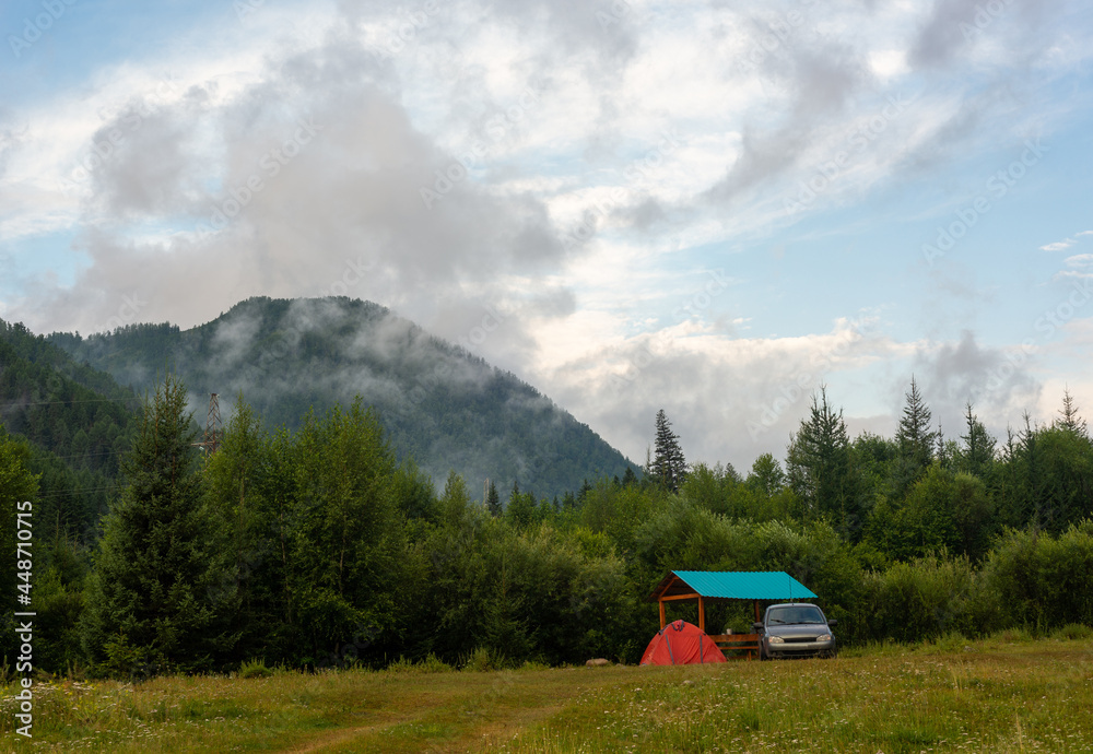 A morning camping scene with a gray car and majestic misty mountains in the background. The concept of travel and camping.
