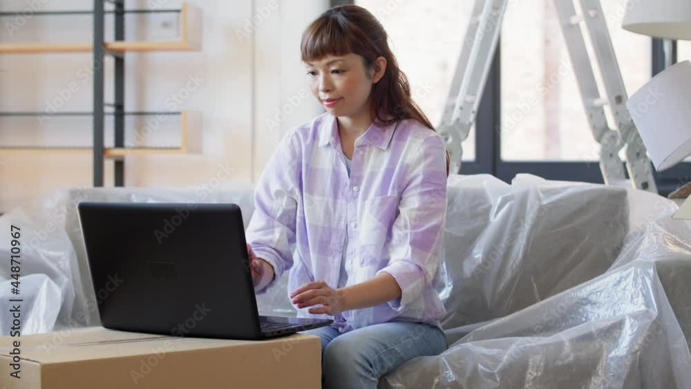 moving, people and real estate concept - happy smiling asian woman with laptop computer and boxes at new home moving, people and real estate concept - happy smiling asian woman with laptop computer and boxes at new home