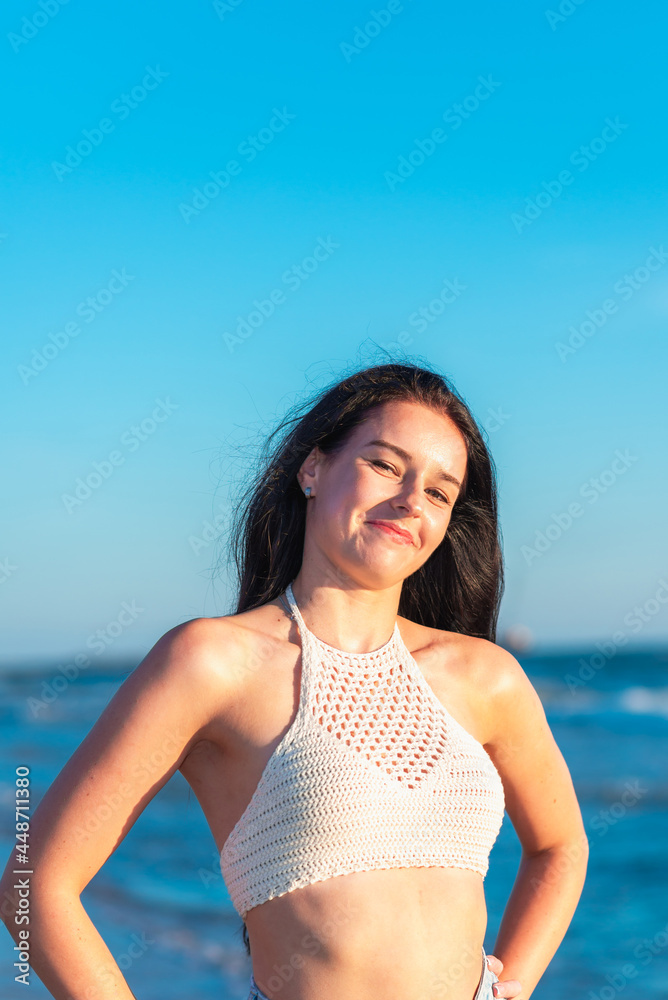 Beautiful sexy girl on the sea beach in a casual clothes looks at the camera at sunset. Nice portrait of model outdoor.