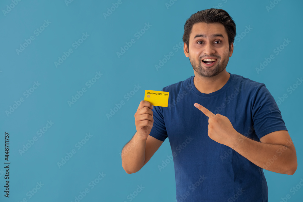A young man pointing towards the credit card in his hand. A young man pointing towards the credit card in his hand.