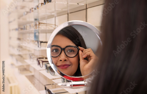 Foto A young woman trying spectacle frames in mirror at an optician's shop