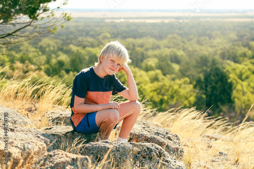 Young boy sitting on rock on hilltop with head resting on hand photo