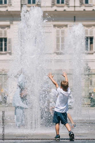 Kid or child playing with water near a fountain during hot summer day, vertical
